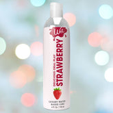 A 4oz bottle of Wet Delicious Oral Play Strawberry Flavored Lube, featuring a red strawberry graphic and brand text on a white label, is shown against a blurred background of colorful lights.
